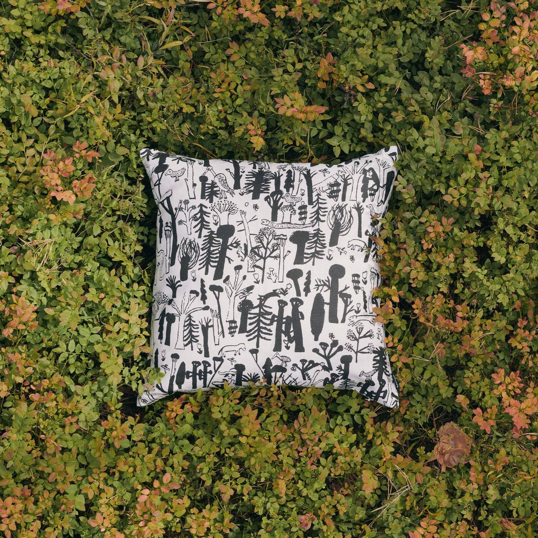 Black forest and animal-pattern linen-cotton cushion cover by Laura Carlin, 18.5" square on a green leafy background.