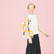 Woman holding a Yellow floral linen-cotton tote bag by Hannele Äijälä, 15" x 17" against a pink background