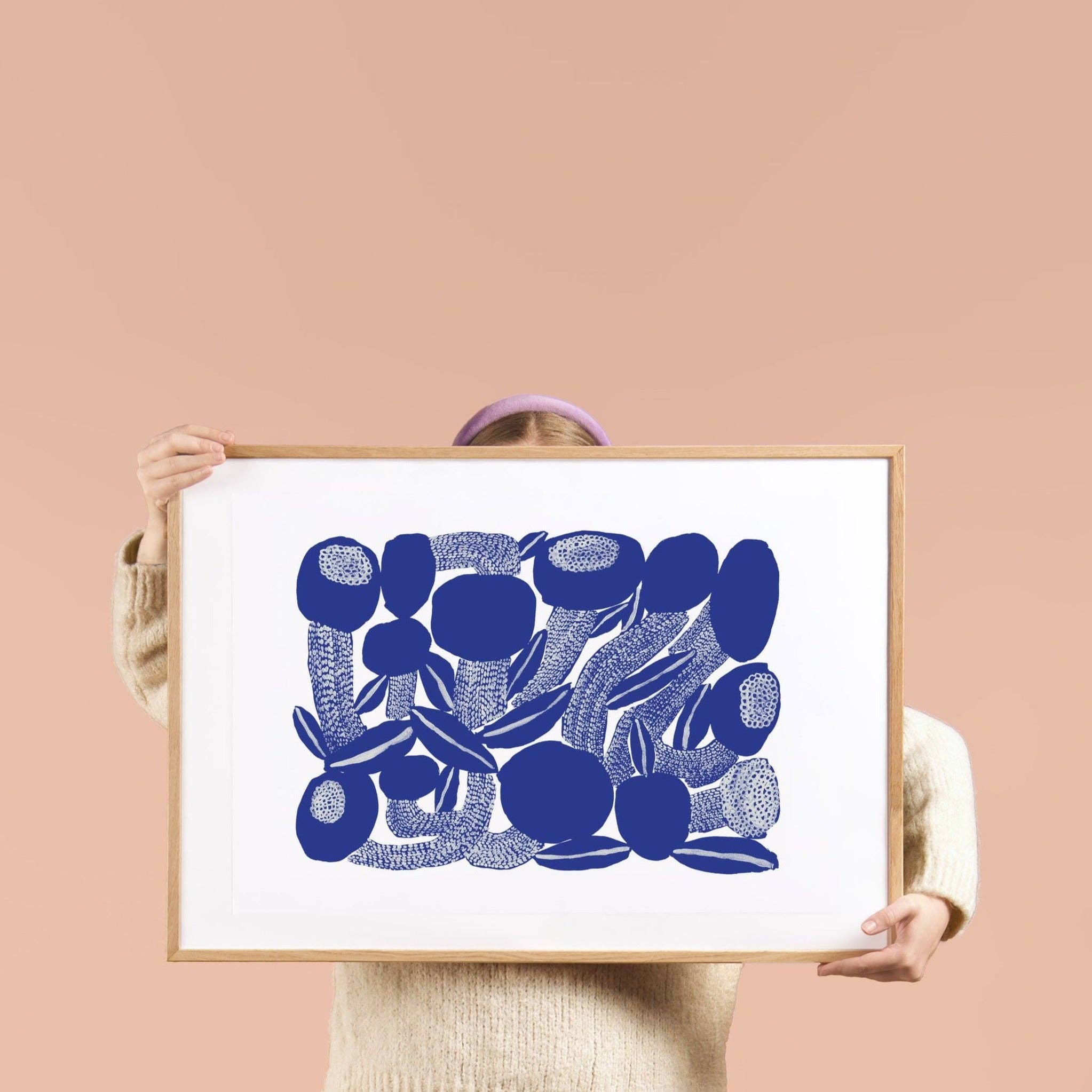 Person holding a framed blue floral watercolor art print by Tong Ren, 27.5" x 19.7", printed on white 170g paper.
 on a pink background
