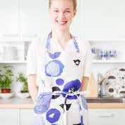 Woman wearing a blue floral and bird-pattern linen-cotton apron by Matti Pikkujämsä.