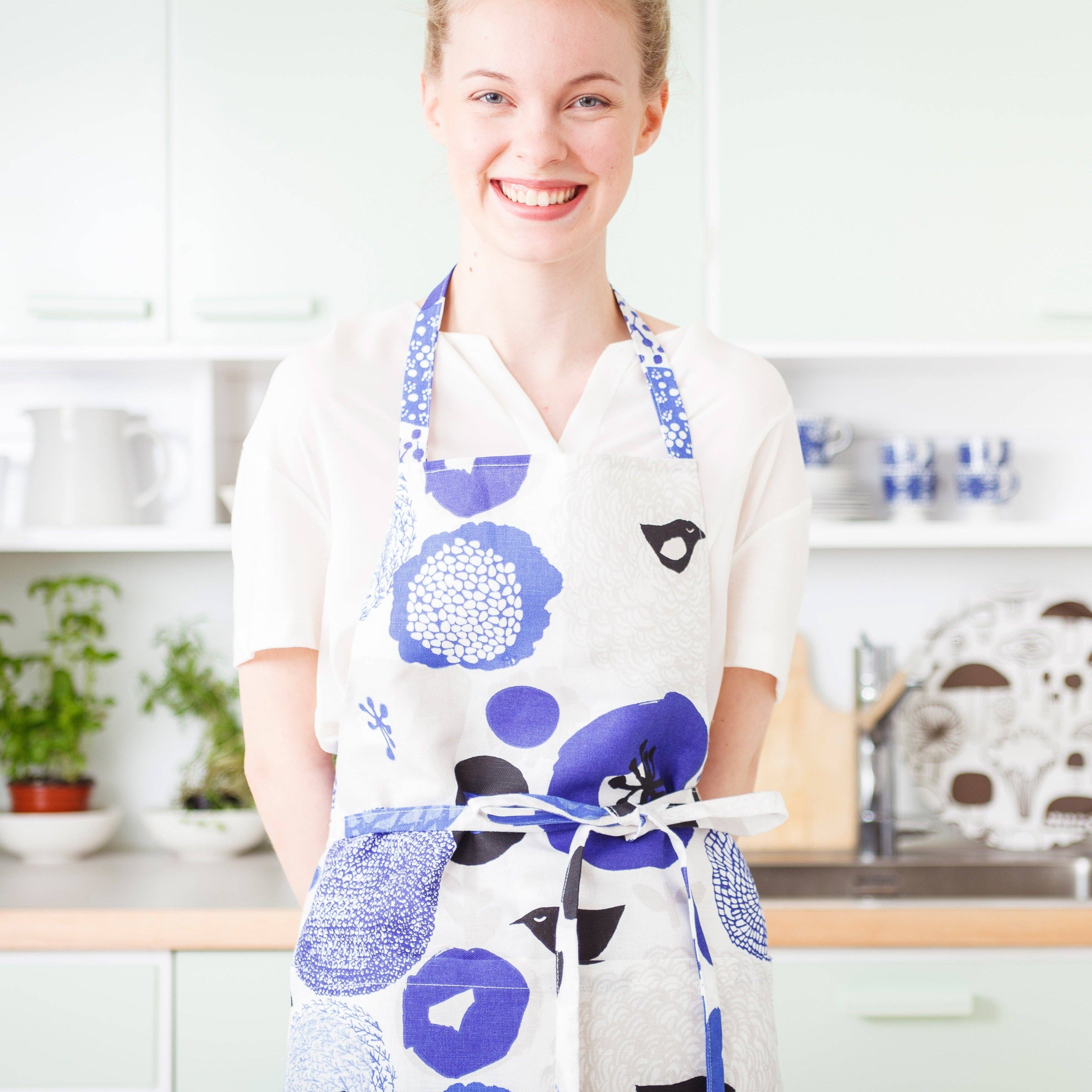 Woman wearing a blue floral and bird-pattern linen-cotton apron by Matti Pikkujämsä.