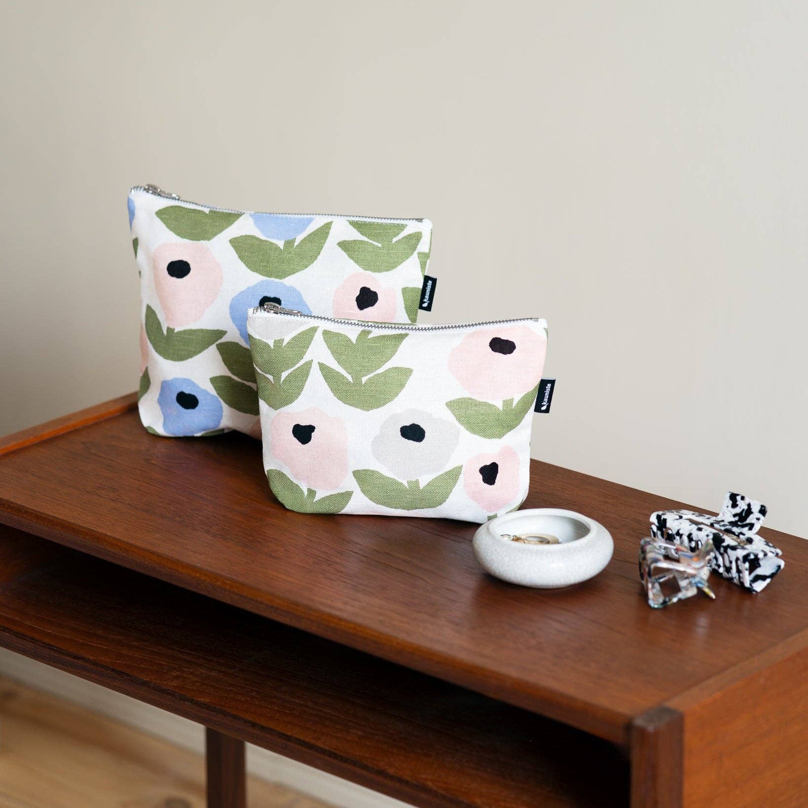 Grey floral linen-cotton zipper pouch by Hannele Äijälä, water-resistant, in two sizes on a wooden surface with a neutral background.