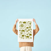 Person holding a Moss green mushroom-pattern linen-cotton kitchen towel by Matti Pikkujämsä against a light blue background.