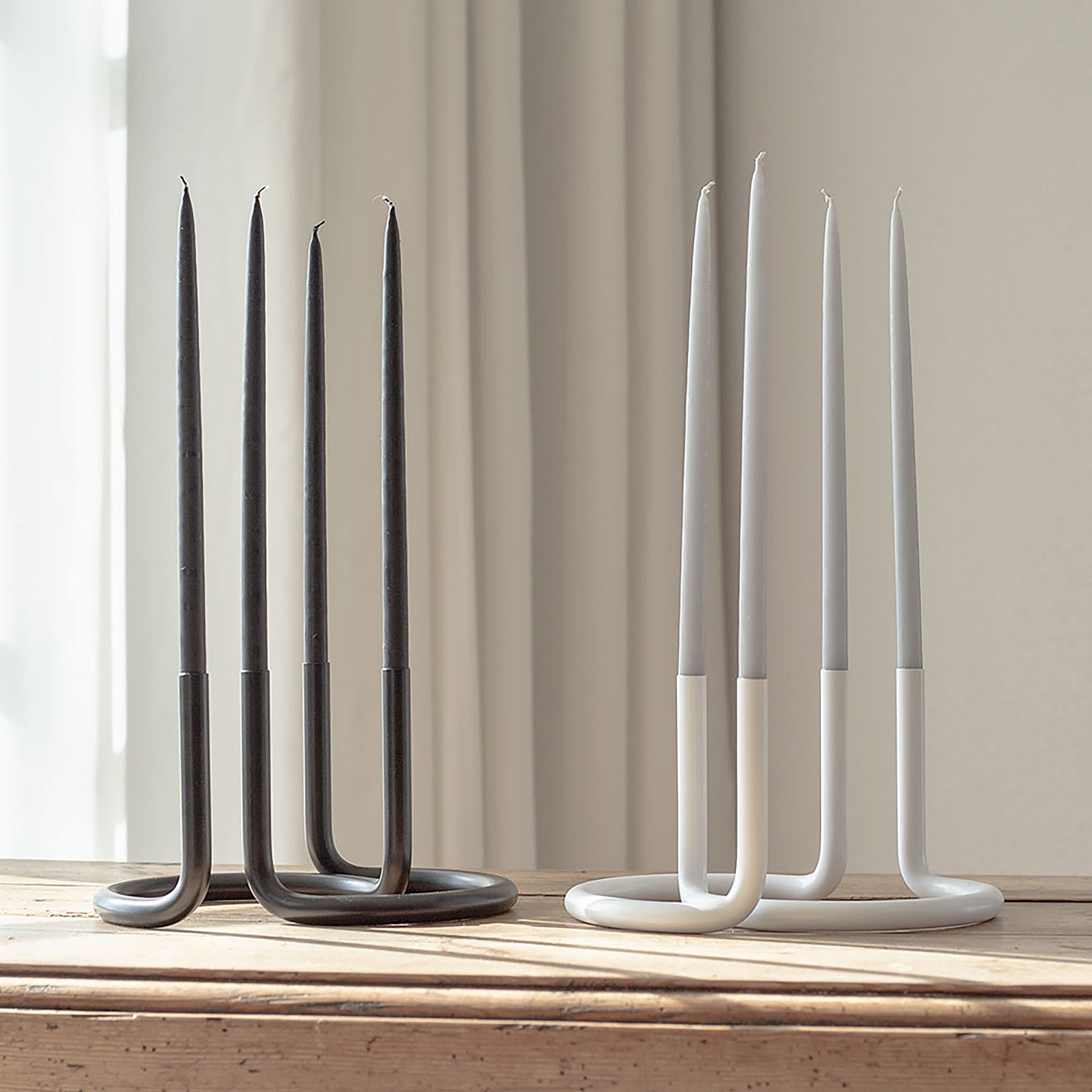Architectmade Gemini Candleholder by Peter Karpf in matte black and matte white stainless steel, styled with matching taper candles in a sculptural curved form.