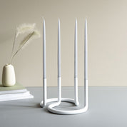Architectmade Gemini Candleholder by Peter Karpf in matte white stainless steel, styled with matching white taper candles in a sculptural curved form.