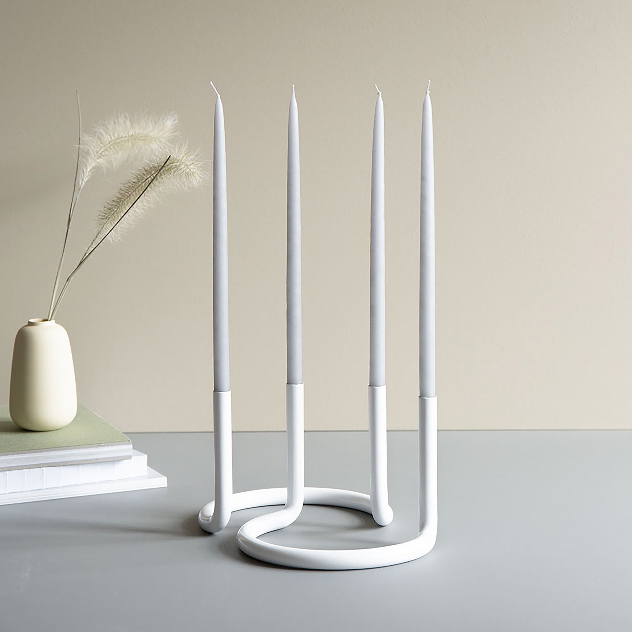 Architectmade Gemini Candleholder by Peter Karpf in matte white stainless steel, styled with matching white taper candles in a sculptural curved form.