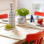 Aveva Design Monday Placemat, 100% wool with embroidered fork, knife, spoon, and plate. Aveva Design Bottle-Vase Cover in 100% wool. Handmade in Nepal—cheeky table setting for everyday meals.