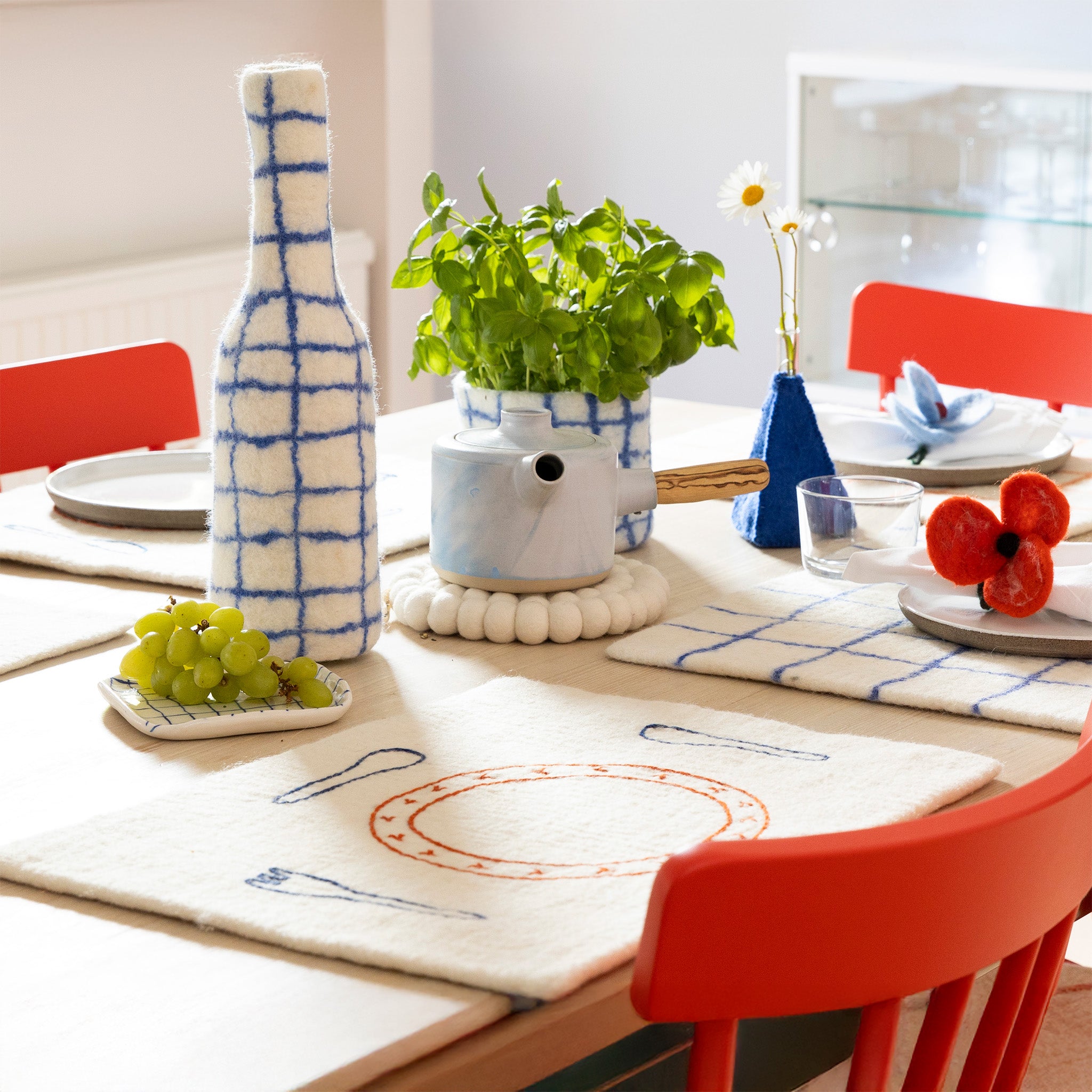 Aveva Design Monday Placemat, 100% wool with embroidered fork, knife, spoon, and plate. Aveva Design Bottle-Vase Cover in 100% wool. Handmade in Nepal—cheeky table setting for everyday meals.