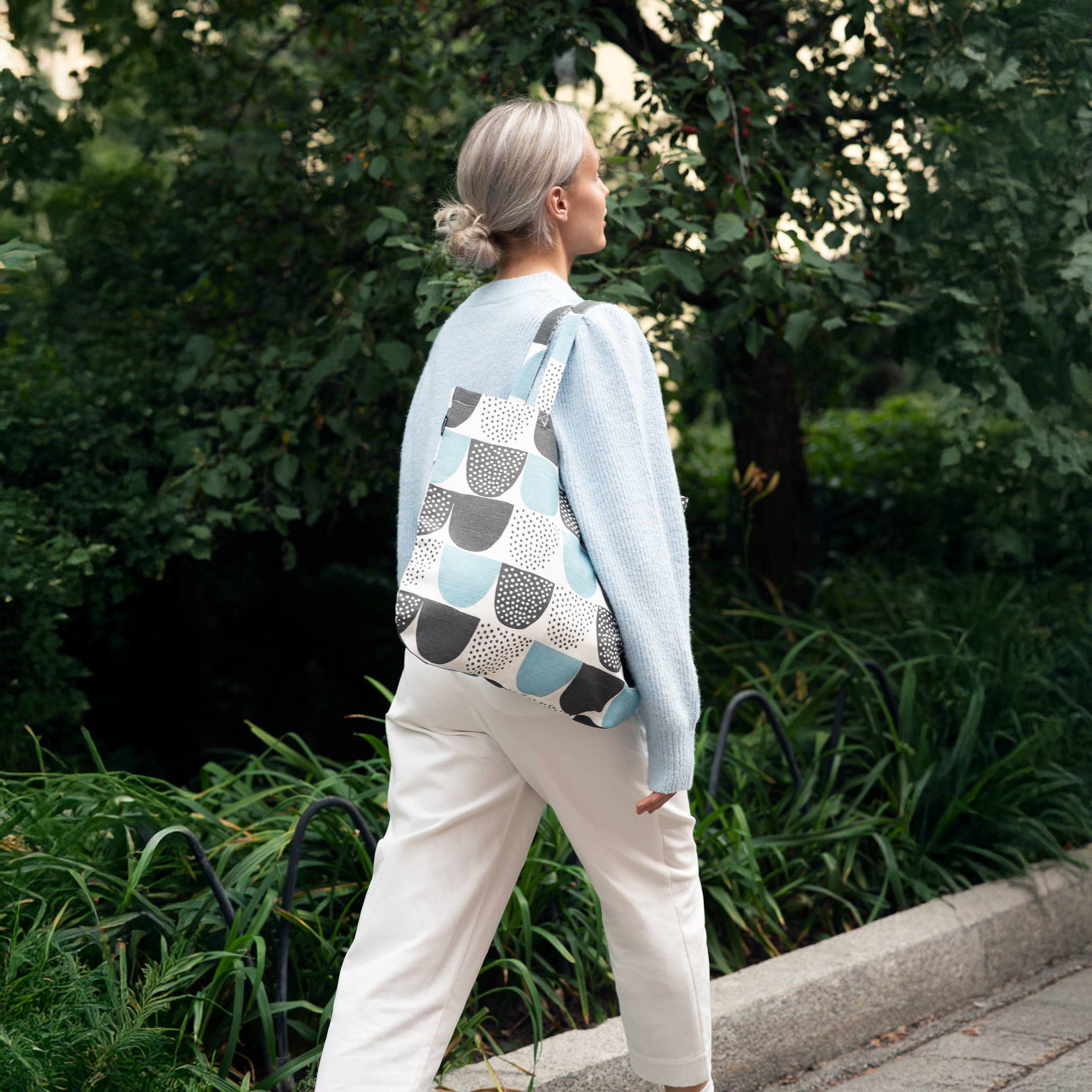 Woman walking outdoors with a light blue and black polka-dot linen-cotton tote bag by Hanna Konola, 15" x 17".