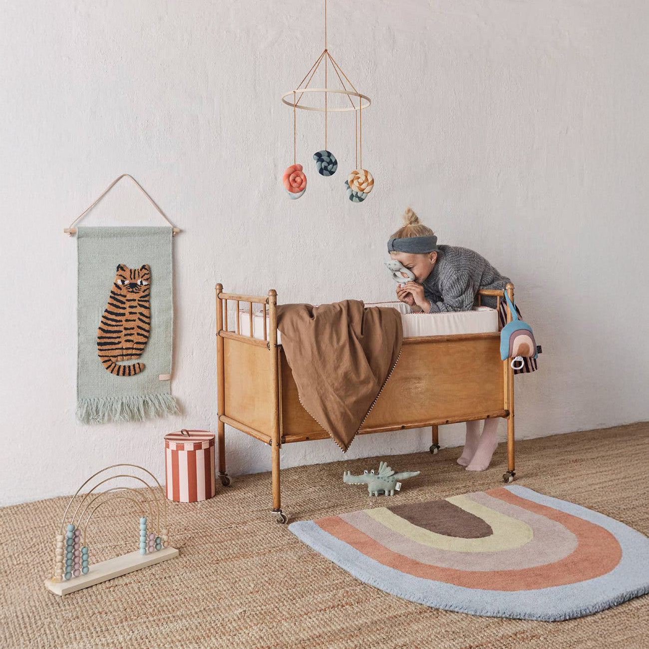 Child in bedroom with OYOY Lollipop Mobile in multi, striped cotton baby nursery mobile with wooden ring.