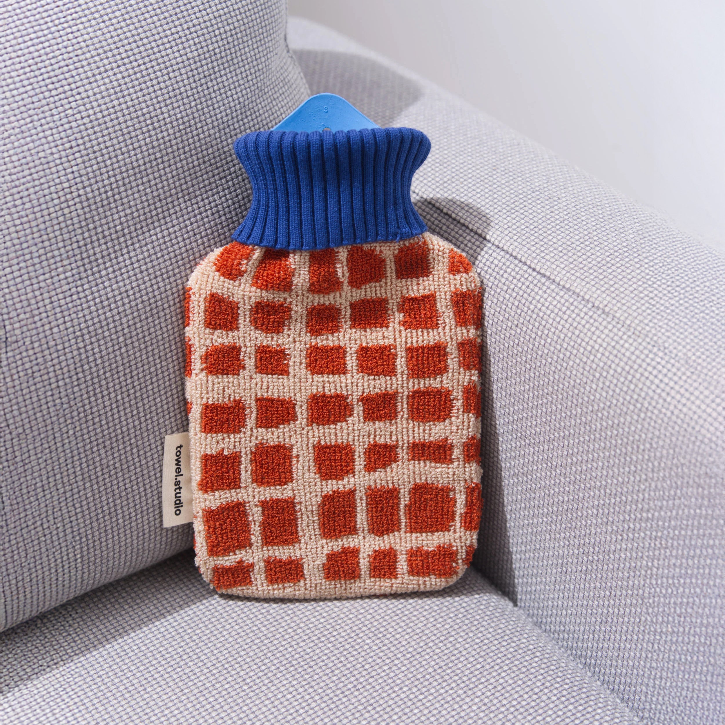 Towel Studio Bold Grid Hot Water Bottle, small 0.8 L. Barn red terry grid cover with blue ribbed collar, organic cotton with natural rubber bottle.